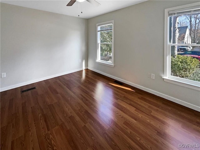 empty room with a ceiling fan, baseboards, visible vents, and dark wood-type flooring