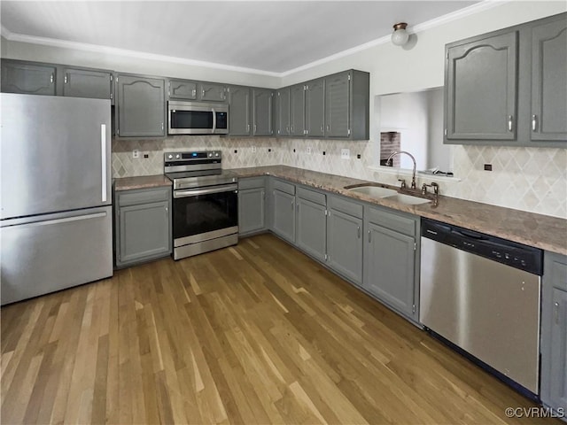 kitchen with stainless steel appliances, a sink, gray cabinetry, and wood finished floors