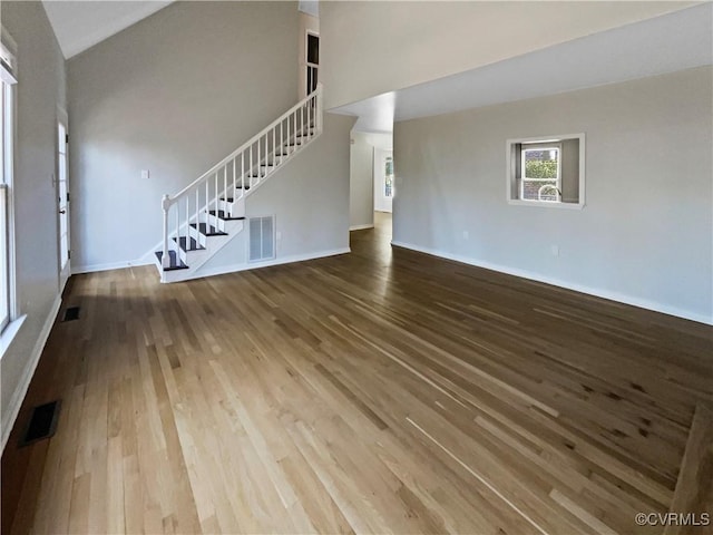 unfurnished living room with wood finished floors, visible vents, and stairs