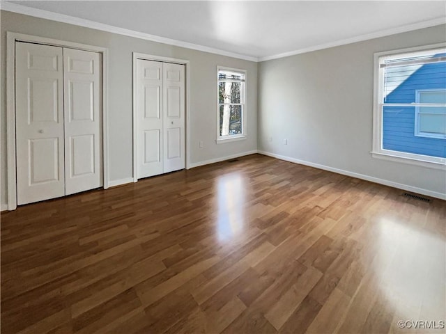 unfurnished bedroom with crown molding, multiple closets, visible vents, dark wood-type flooring, and baseboards