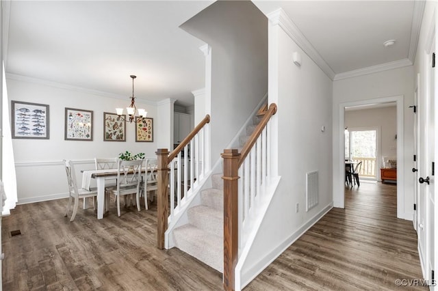 staircase featuring ornamental molding, visible vents, an inviting chandelier, and wood finished floors