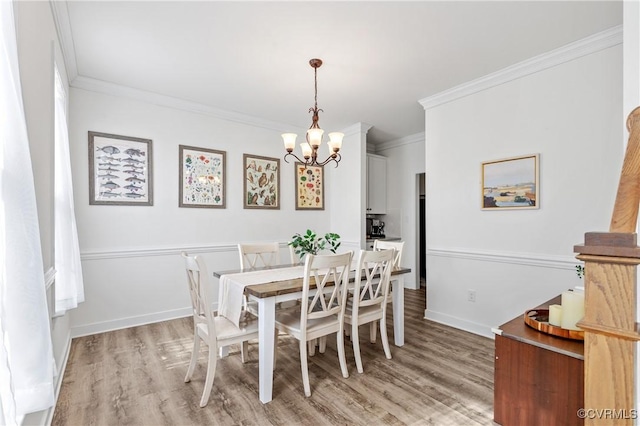 dining space with light wood-style floors, baseboards, ornamental molding, and an inviting chandelier