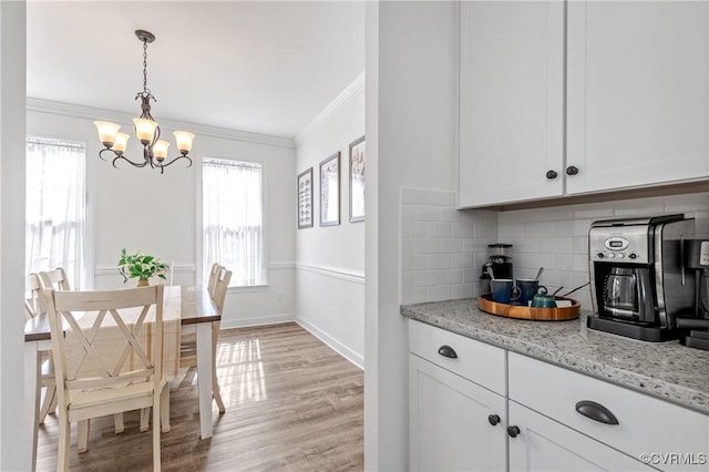 kitchen featuring crown molding, white cabinetry, light wood-style floors, tasteful backsplash, and pendant lighting