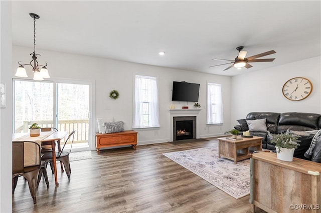 living room featuring a fireplace with flush hearth, baseboards, wood finished floors, and ceiling fan with notable chandelier