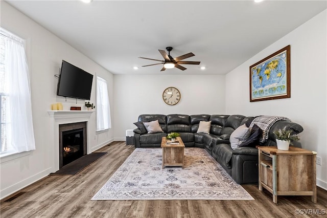 living area with a glass covered fireplace, wood finished floors, visible vents, and baseboards