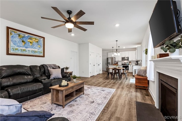 living area featuring ceiling fan, recessed lighting, a fireplace with flush hearth, wood finished floors, and baseboards