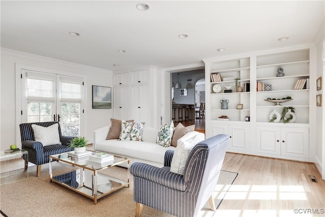 living area featuring arched walkways, visible vents, light wood finished floors, and ornamental molding