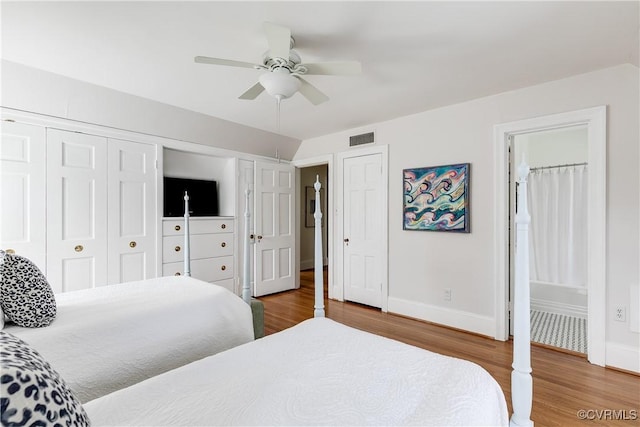 bedroom featuring visible vents, multiple closets, a ceiling fan, wood finished floors, and baseboards