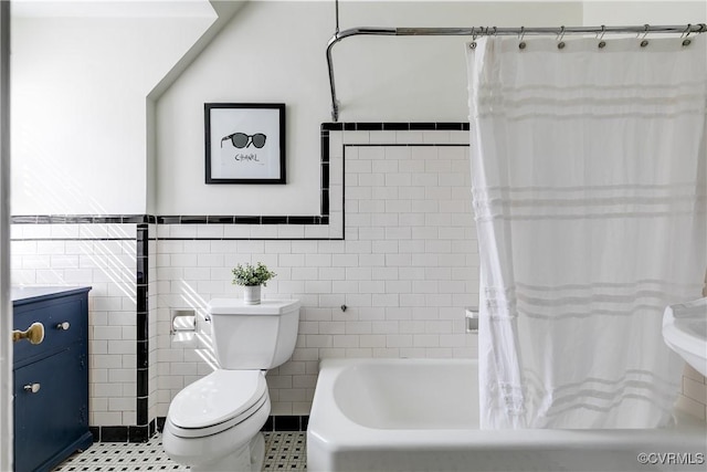 full bathroom featuring a wainscoted wall, toilet, shower / bath combo with shower curtain, tile patterned floors, and tile walls