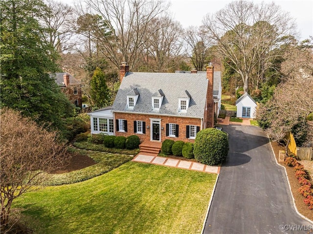 cape cod-style house with brick siding, driveway, a chimney, and a front yard