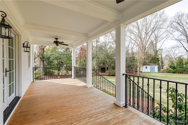 wooden terrace featuring an outbuilding, a storage unit, a ceiling fan, and a lawn