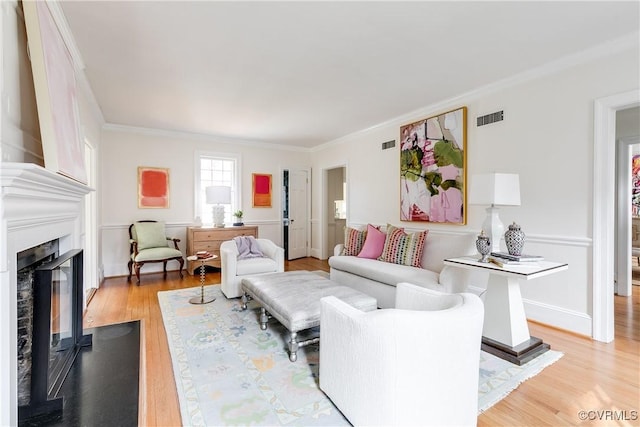 living room with visible vents, light wood-style floors, a glass covered fireplace, and crown molding