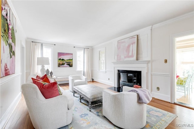 living room featuring a glass covered fireplace, ornamental molding, baseboards, and wood finished floors