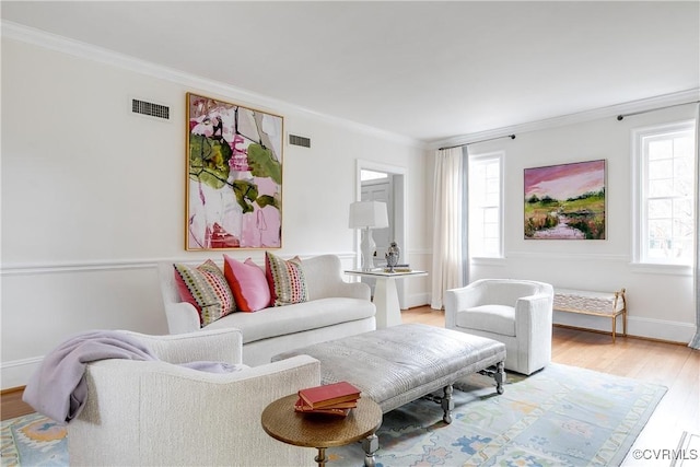 living room featuring visible vents, baseboards, ornamental molding, and light wood-style flooring