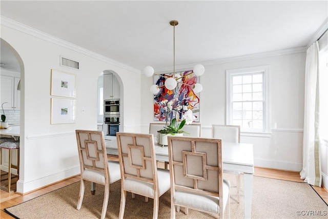 dining space featuring light wood-type flooring, visible vents, ornamental molding, arched walkways, and baseboards