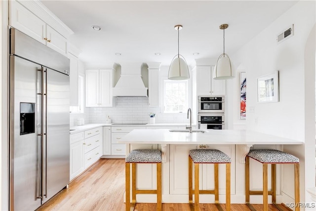 kitchen featuring a breakfast bar, stainless steel appliances, custom range hood, and a sink