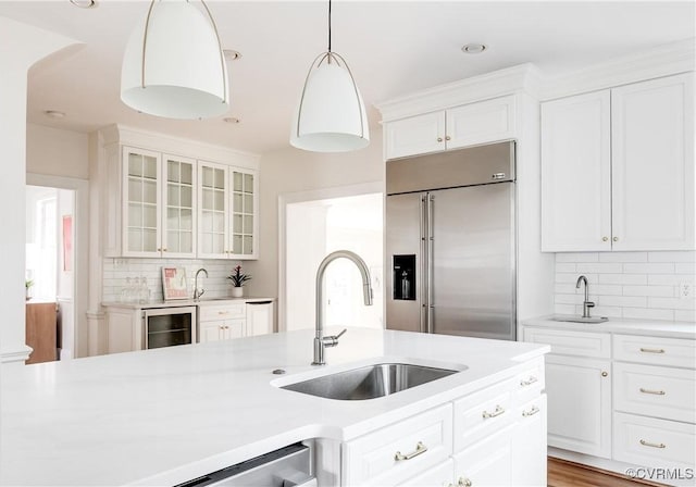 kitchen with glass insert cabinets, wine cooler, built in refrigerator, light countertops, and a sink