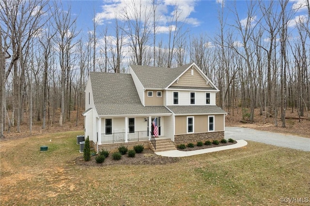 craftsman-style house featuring a porch, a front yard, roof with shingles, stone siding, and driveway