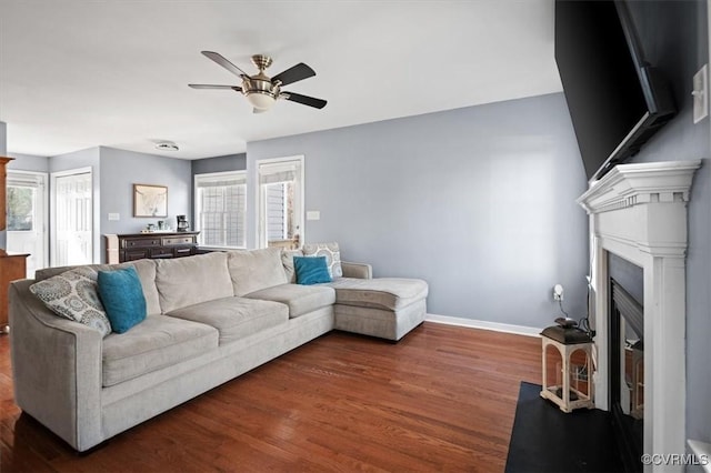 living area with a ceiling fan, a fireplace, baseboards, and wood finished floors