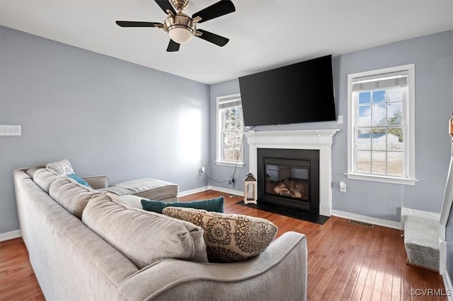 living room with baseboards, visible vents, a ceiling fan, a fireplace with flush hearth, and hardwood / wood-style floors