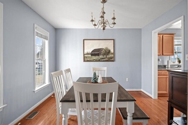 dining space with light wood-style floors, a wealth of natural light, visible vents, and an inviting chandelier