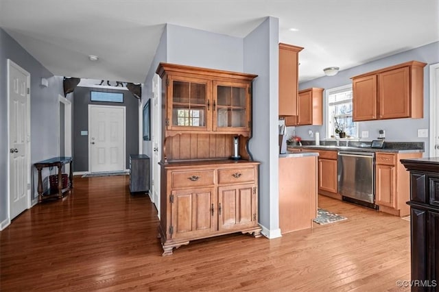 kitchen with stainless steel dishwasher, dark countertops, light wood-style flooring, and baseboards