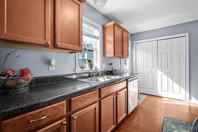 kitchen with brown cabinets, dark countertops, a sink, wood finished floors, and dishwasher