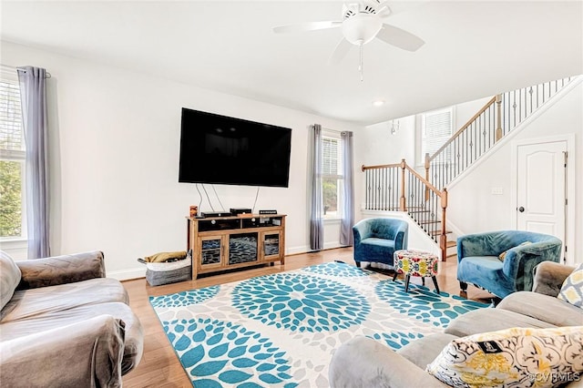 living room with a ceiling fan, stairway, baseboards, and wood finished floors