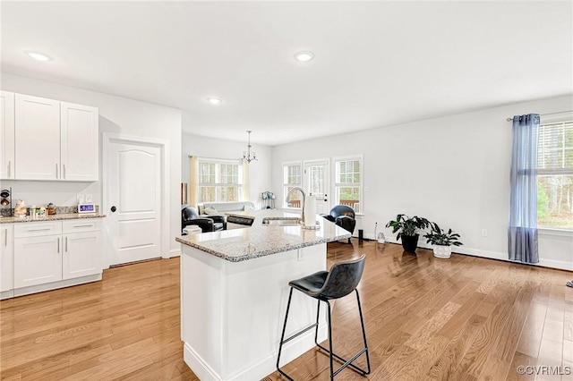 kitchen featuring light wood-style flooring, a kitchen bar, white cabinetry, and a sink