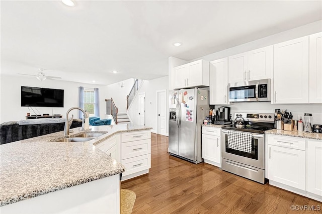 kitchen with white cabinets, appliances with stainless steel finishes, open floor plan, wood finished floors, and a sink