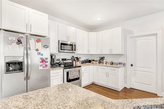 kitchen with appliances with stainless steel finishes, light stone counters, wood finished floors, white cabinetry, and recessed lighting