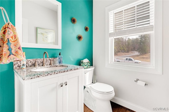 half bathroom with baseboards, vanity, toilet, and wood finished floors