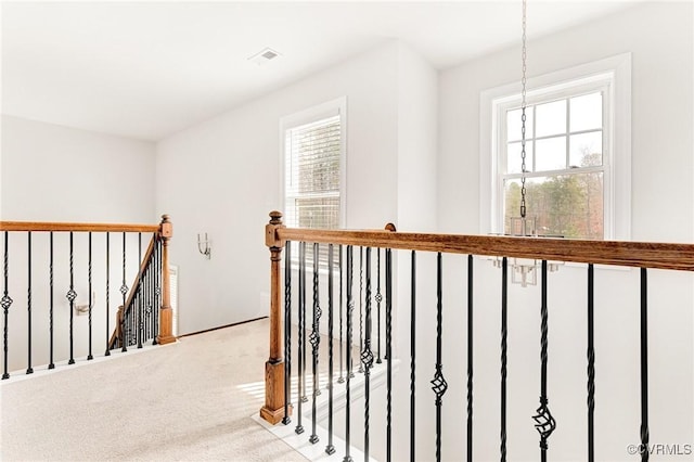 hall featuring a healthy amount of sunlight, visible vents, carpet flooring, and an upstairs landing