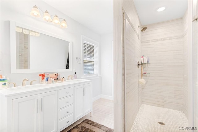 bathroom featuring double vanity, a tile shower, and a sink