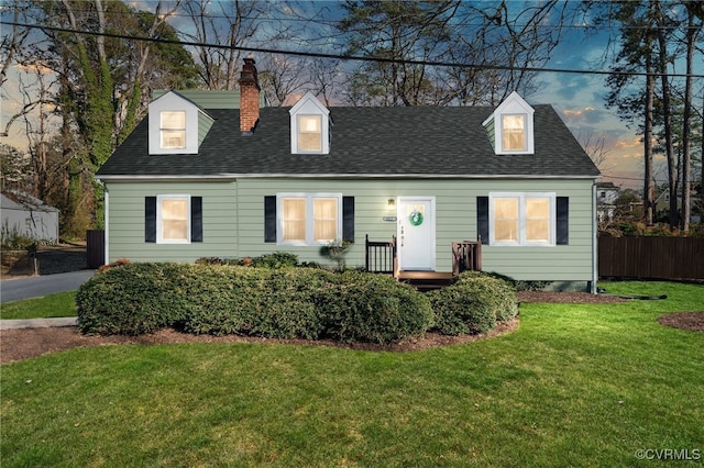 cape cod house with a chimney, a lawn, a shingled roof, and fence