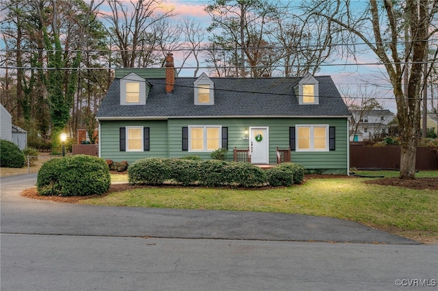 cape cod-style house with a front yard, fence, roof with shingles, and a chimney