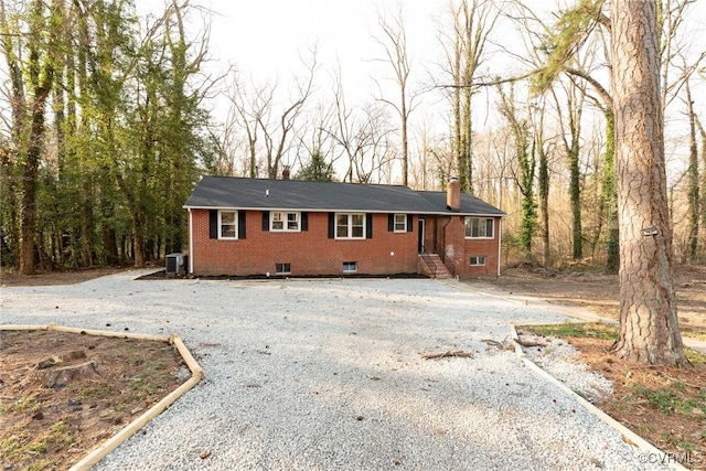 ranch-style home featuring brick siding, a chimney, central AC unit, and gravel driveway