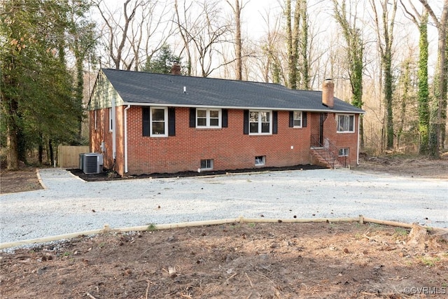 rear view of property with brick siding, driveway, a chimney, and central air condition unit