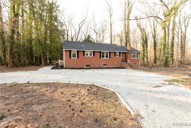 ranch-style house featuring central air condition unit, a chimney, and brick siding