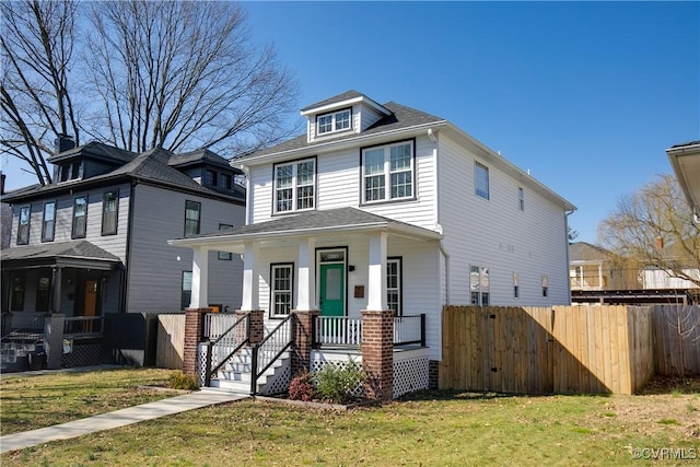 traditional style home with covered porch, fence, and a front lawn