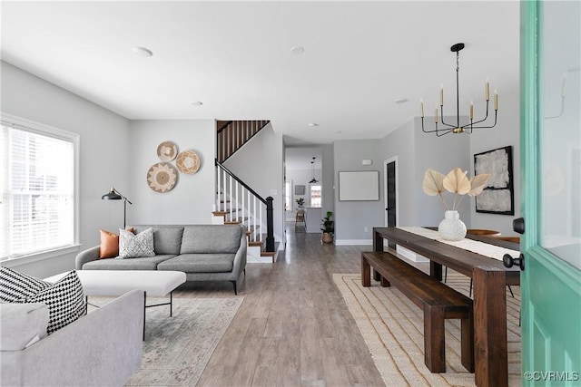 living room featuring light wood-type flooring, stairs, baseboards, and a notable chandelier