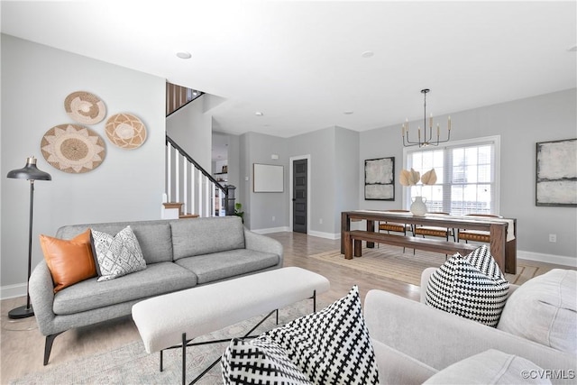 living room with stairs, light wood-type flooring, a notable chandelier, and baseboards