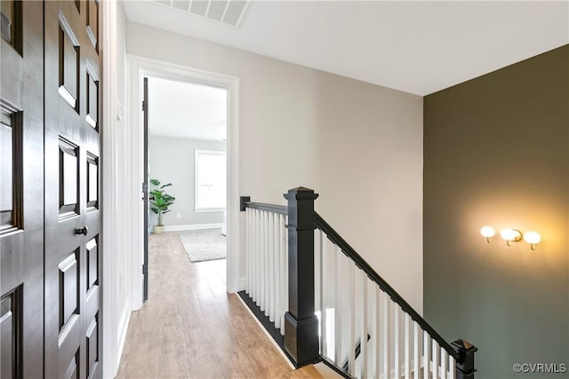 corridor with baseboards, visible vents, light wood finished floors, and an upstairs landing