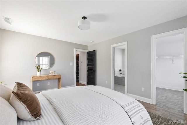 bedroom with baseboards, visible vents, connected bathroom, wood finished floors, and a spacious closet