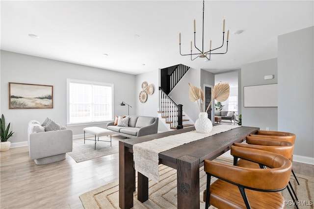 dining area with stairs, light wood finished floors, baseboards, and an inviting chandelier