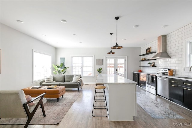 kitchen featuring french doors, stainless steel appliances, a kitchen bar, a sink, and wall chimney exhaust hood