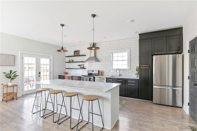 kitchen featuring stainless steel appliances, french doors, backsplash, wall chimney exhaust hood, and a kitchen bar