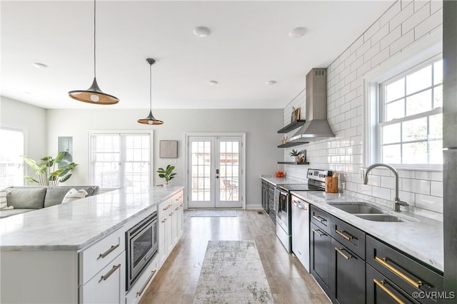 kitchen with open shelves, stainless steel appliances, a sink, french doors, and wall chimney exhaust hood