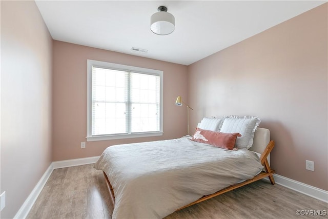 bedroom with baseboards, visible vents, and wood finished floors