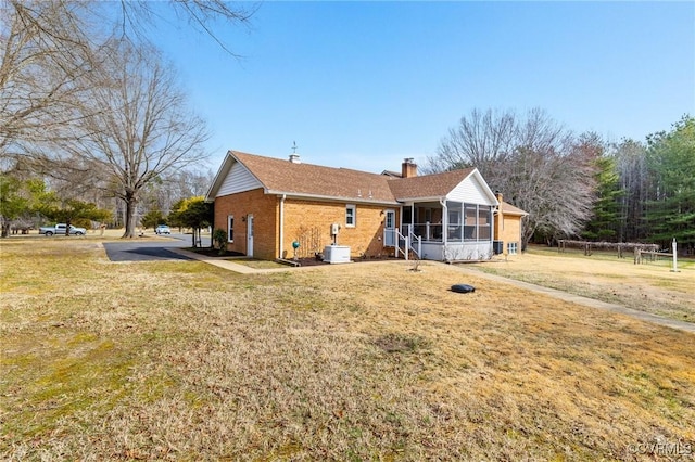 back of property with a yard, a sunroom, a chimney, and brick siding